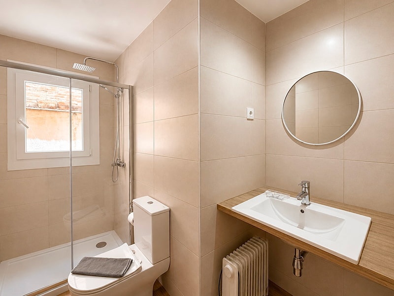 Baño moderno equipado con ducha de cristal, lavabo amplio y espejo redondo