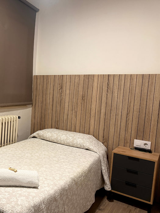 Habitación individual con cama cómoda y  pared de madera