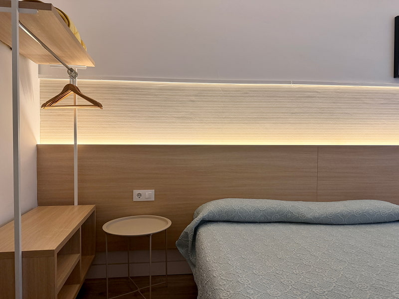 Cama individual con iluminación ambiental y detalles en madera clara
